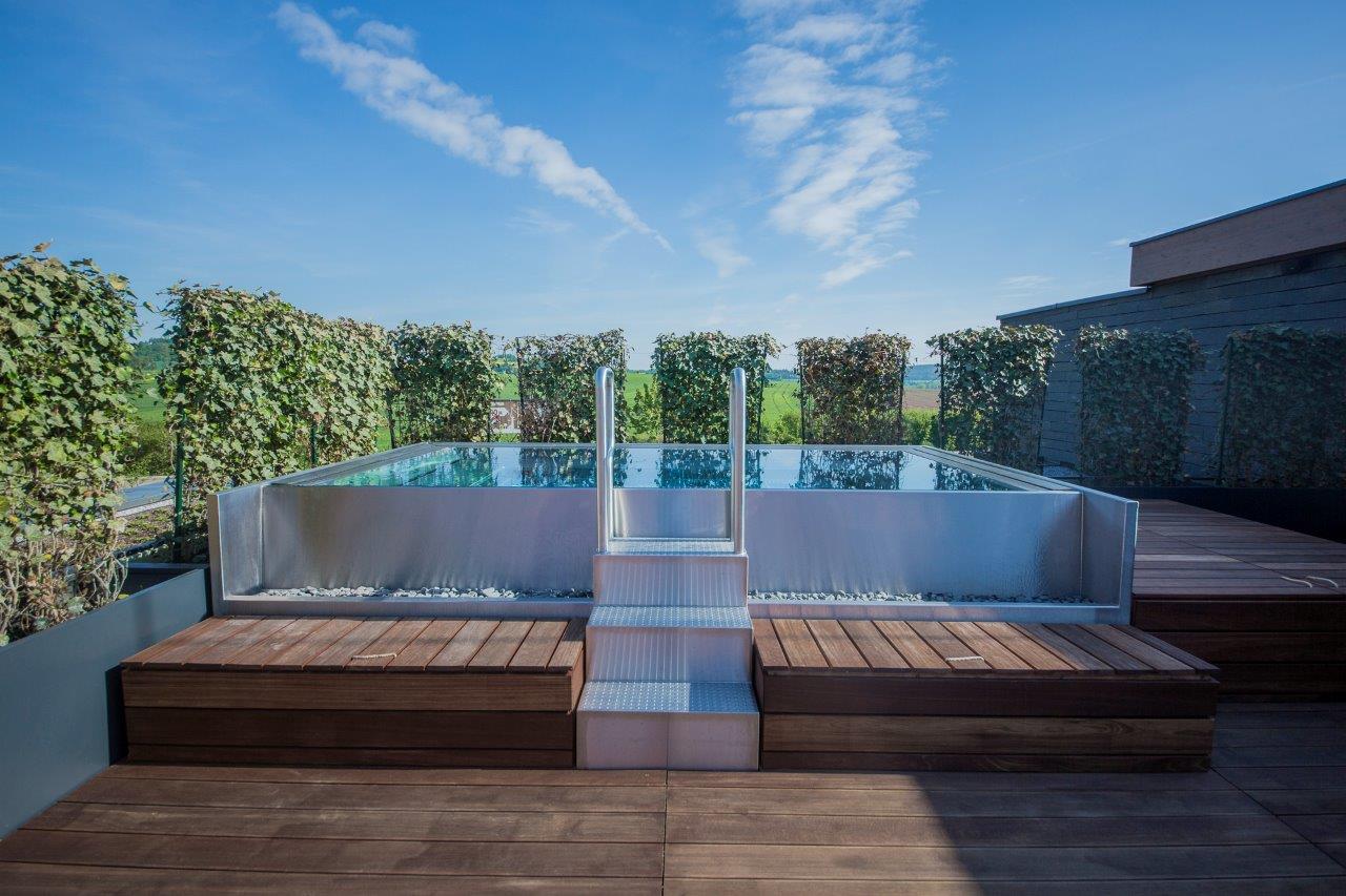 Piscina exterior em inox com acesso por escada. Referência de integração na paisagem.